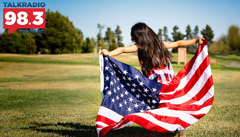 Girl holding U.S. flag, running in field