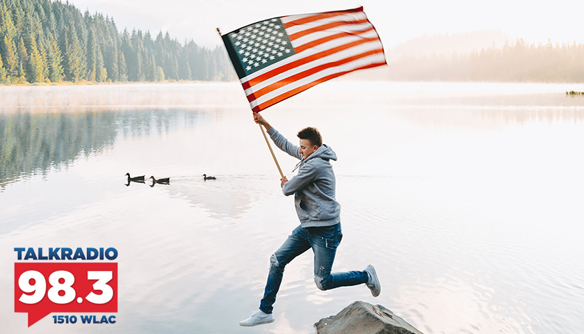 Man leaping onto rocks in lack, holding American flag